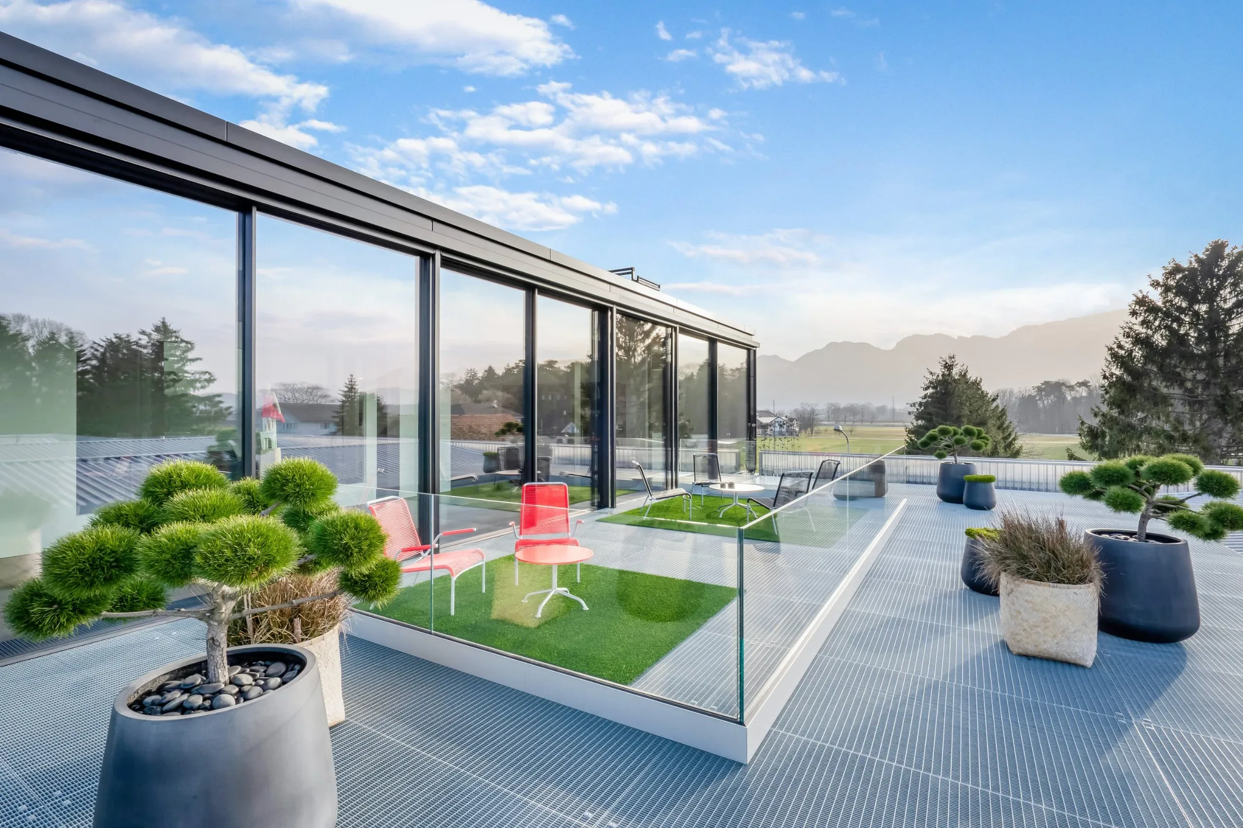 Offene Dachterasse mit farbigen Loungestühlen im Hintergrund eine Sky-frame Verglasung und im Vordergrund eine Ganzglasgeländer, vorher