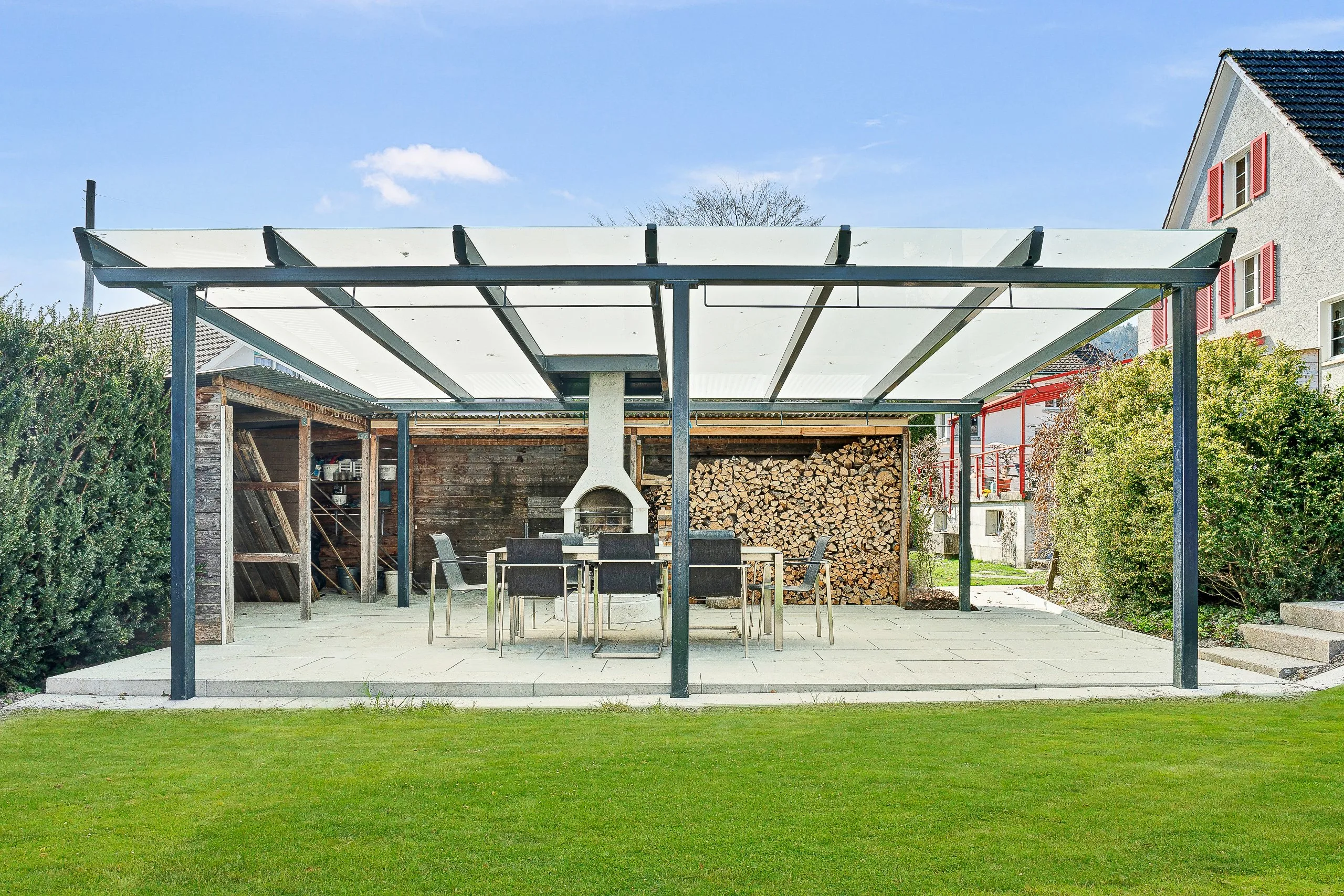 Frontalansicht einer Gartensitzplatzüberdachung mit satiniertem Glas und im Glasdach ausgeschnittenen Cheminéet.