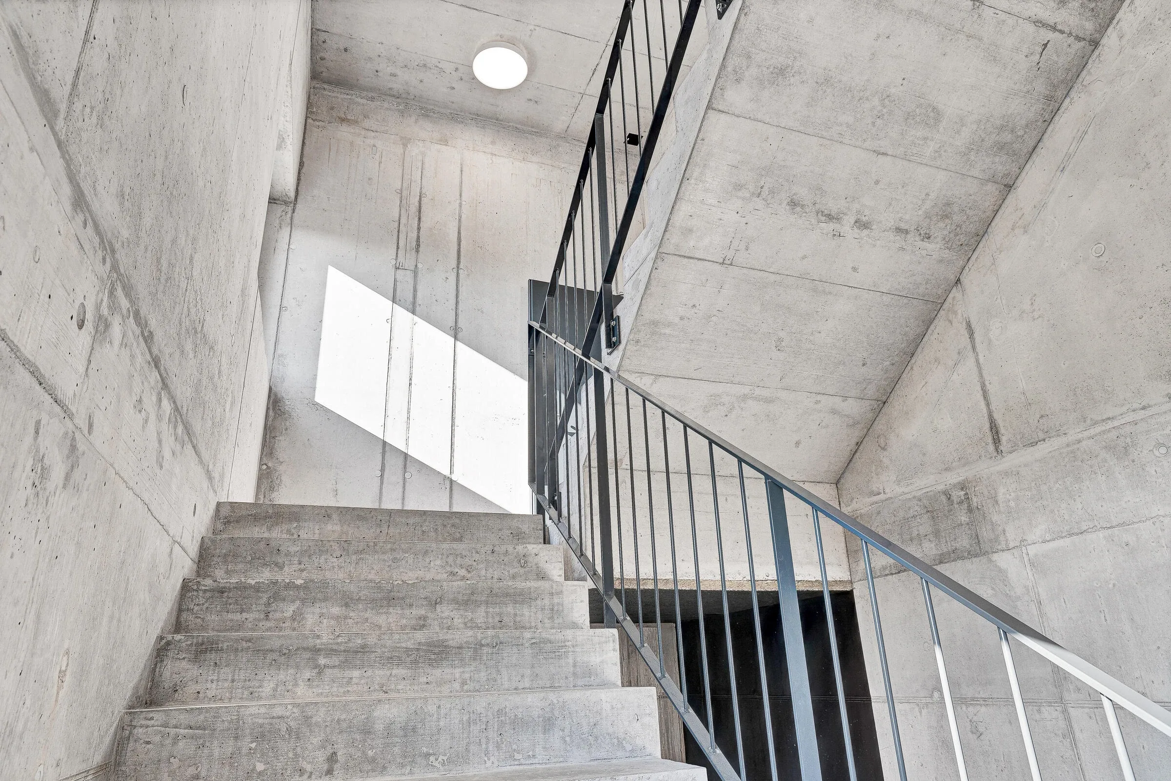 Treppenhaus innen mit Betonstufen und dunklem Metallrohr-Gelaender