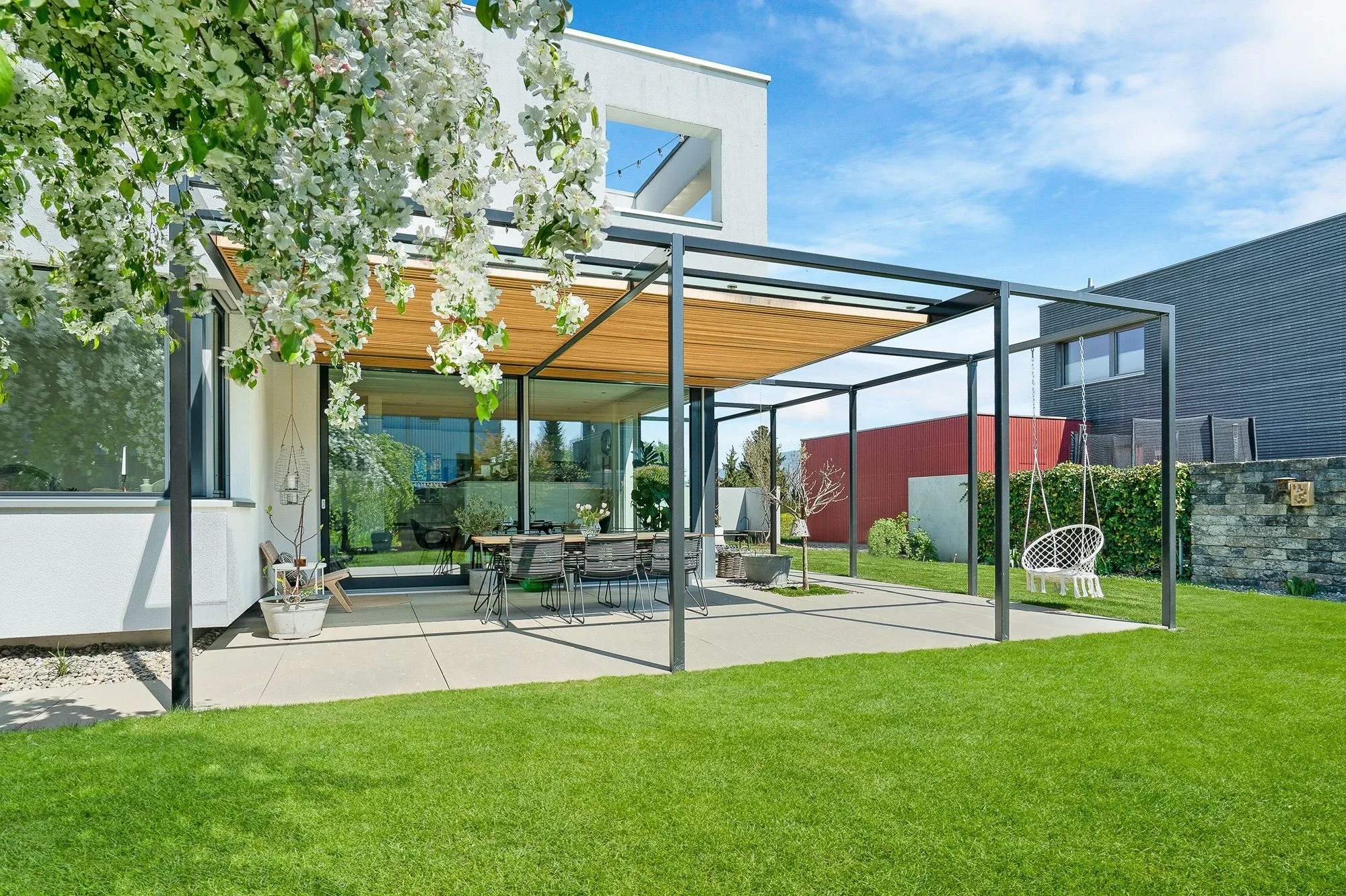 Blick auf eine moderne Sitzplatzkonstruktion aus Metall mit Glasdach in Kombination mit Holzlatten welche als Sonnenschutz dienen