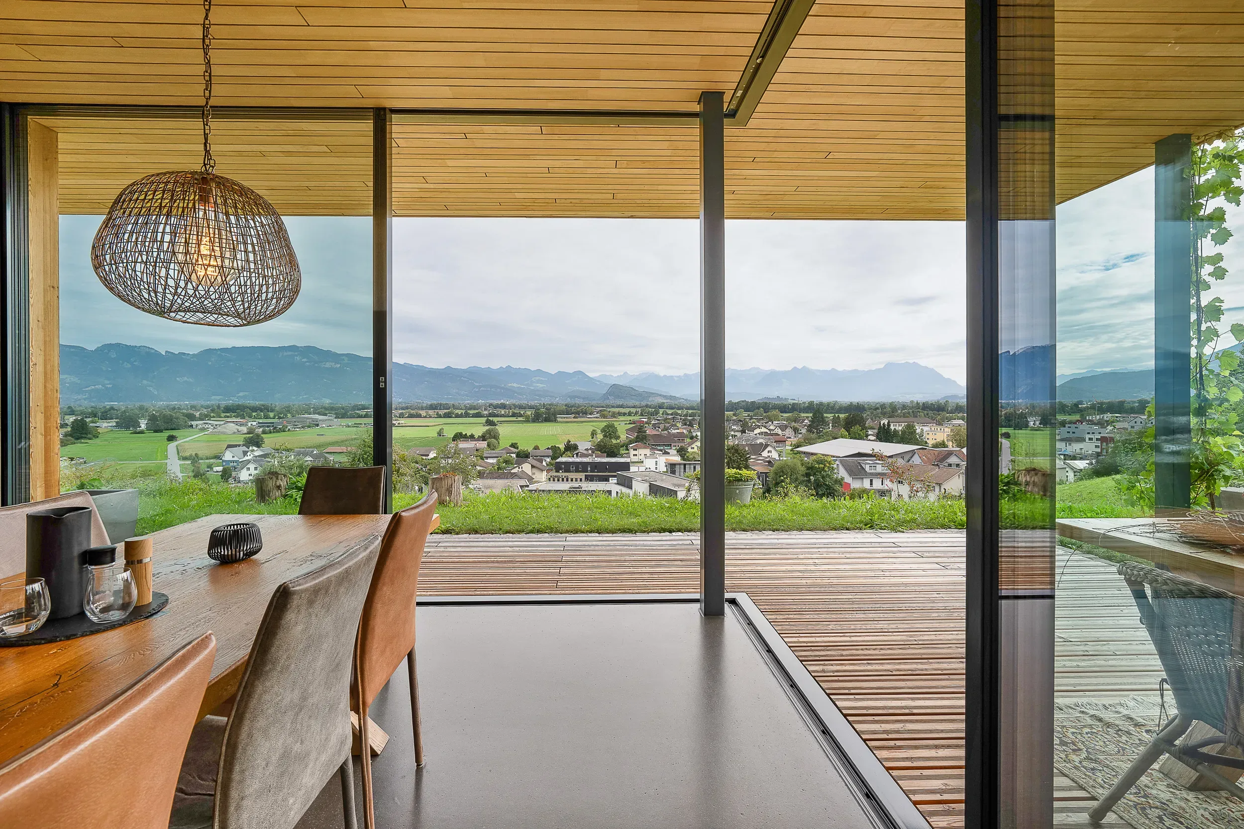 Blick vom Esstisch durch bodentiefe Sky-Frame-Verglasung auf Terrasse und Alpen