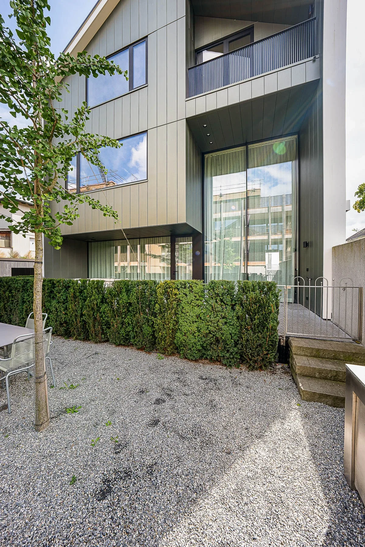 Aussenansicht Erdgeschoss mit raumhoher Verglasung, Hecke und Seitentreppe