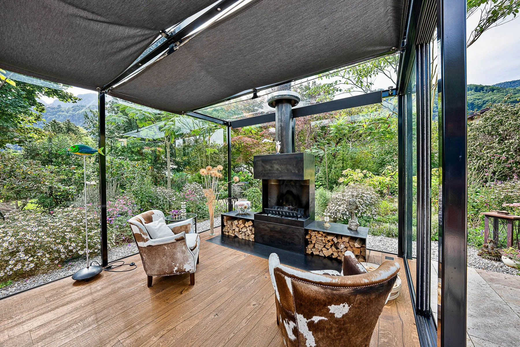 Frontale Gesamtansicht der Glaslounge mit Gartenumgebung und Wolkenhimmel
