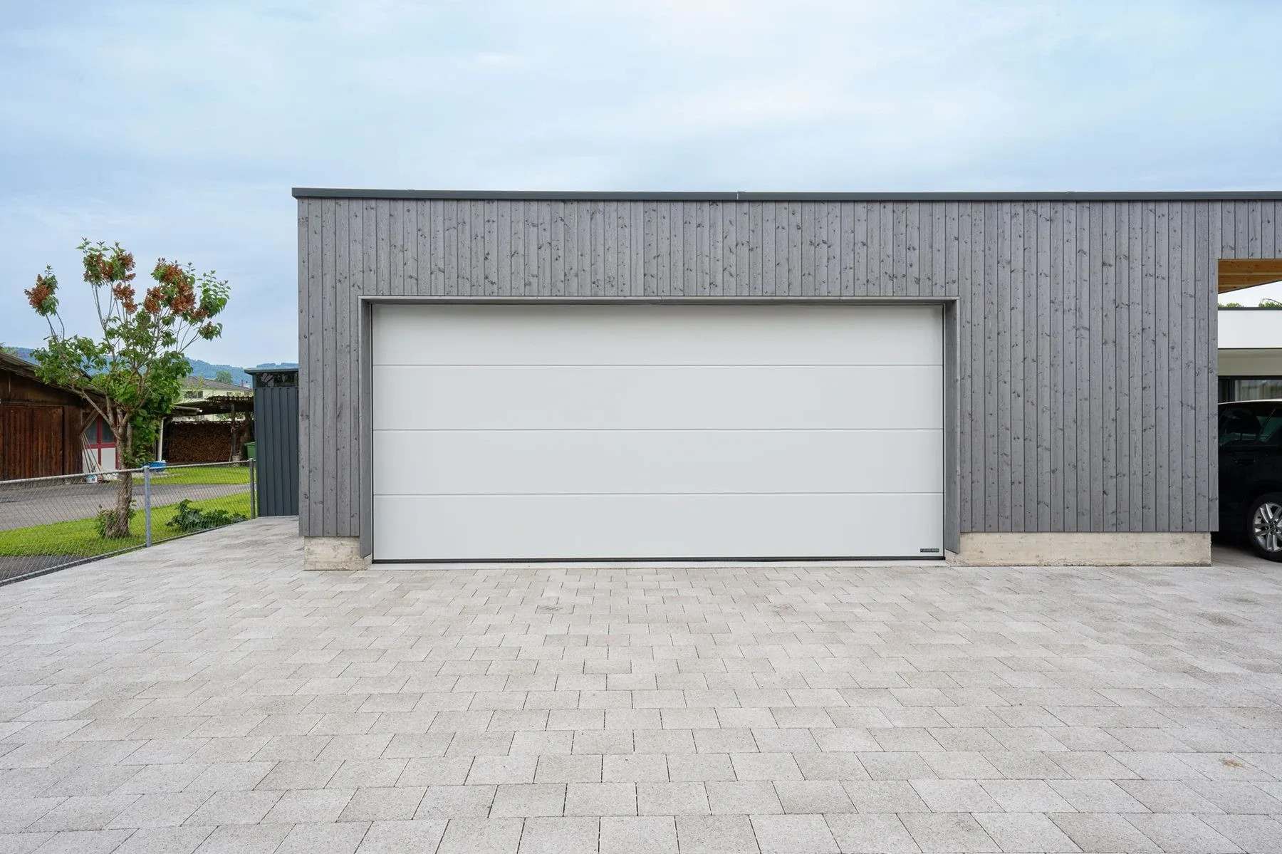 helles Sektionaltor an einem mit Holz verkleideten Carport