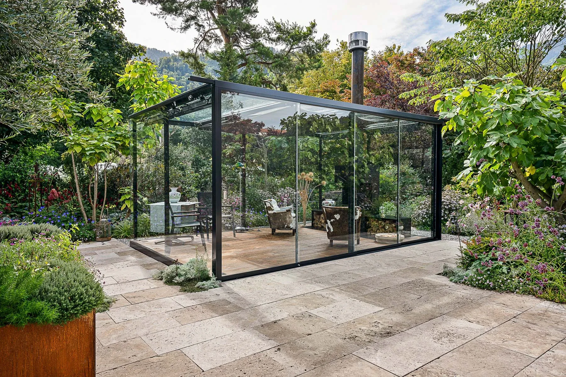 Innenansicht der Lounge mit Cheminee, Kuhfell-Sesseln und geoeffneten Glaswaenden zum Garten