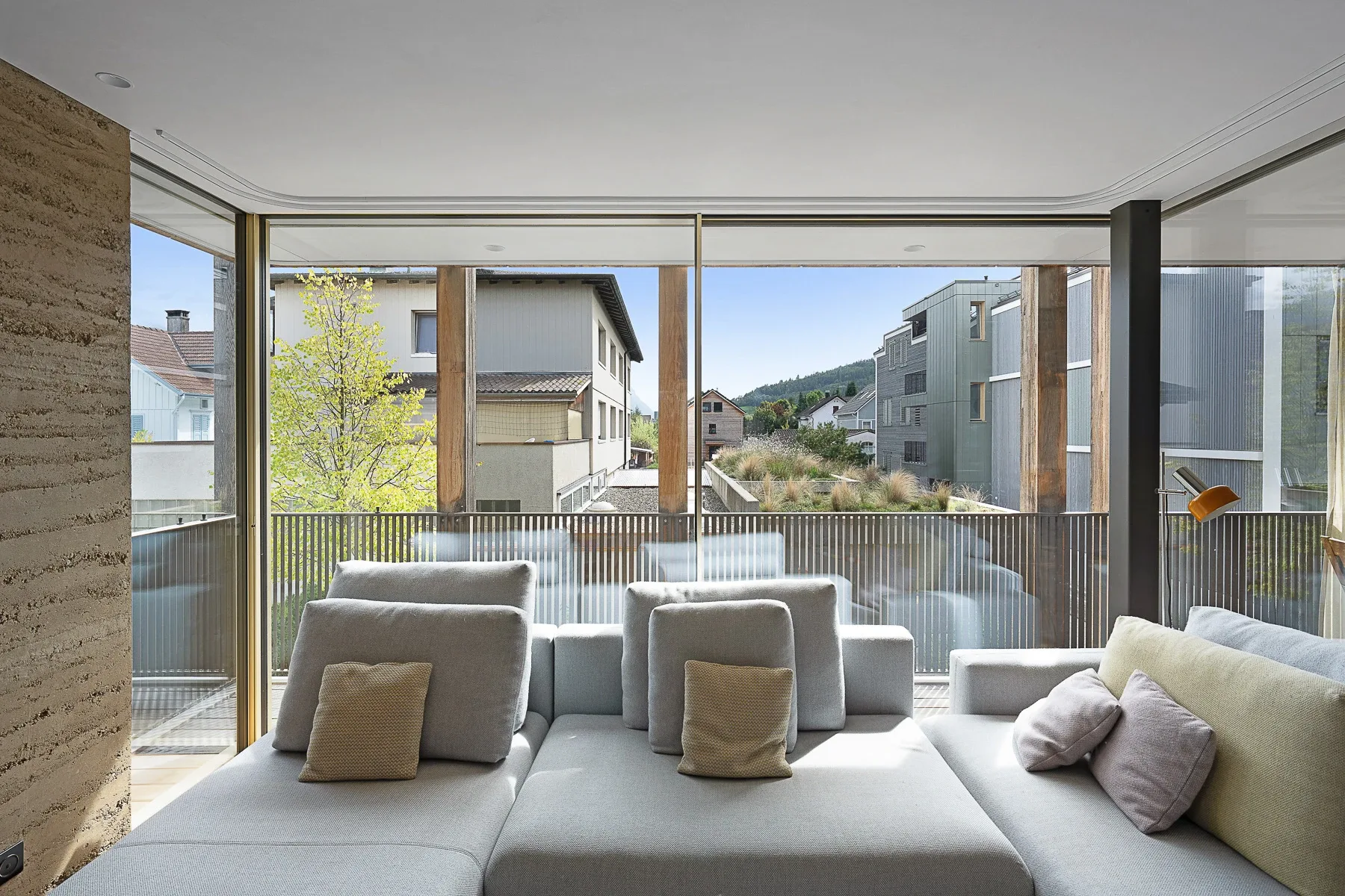 Loft-Innenansicht mit Sofa-Landschaft und raumhoher Sky-Frame Verglasung zum Balkon