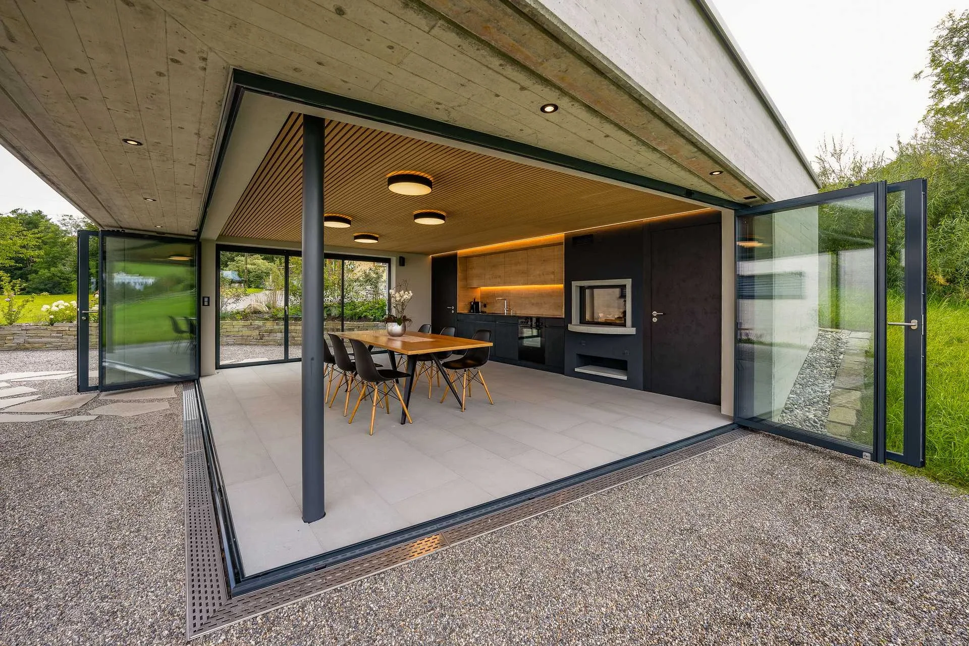 Pavillon frontal mit offener Verglasung, Esstisch mit Deckenleuchten und Sichtbeton-Ueberdachung