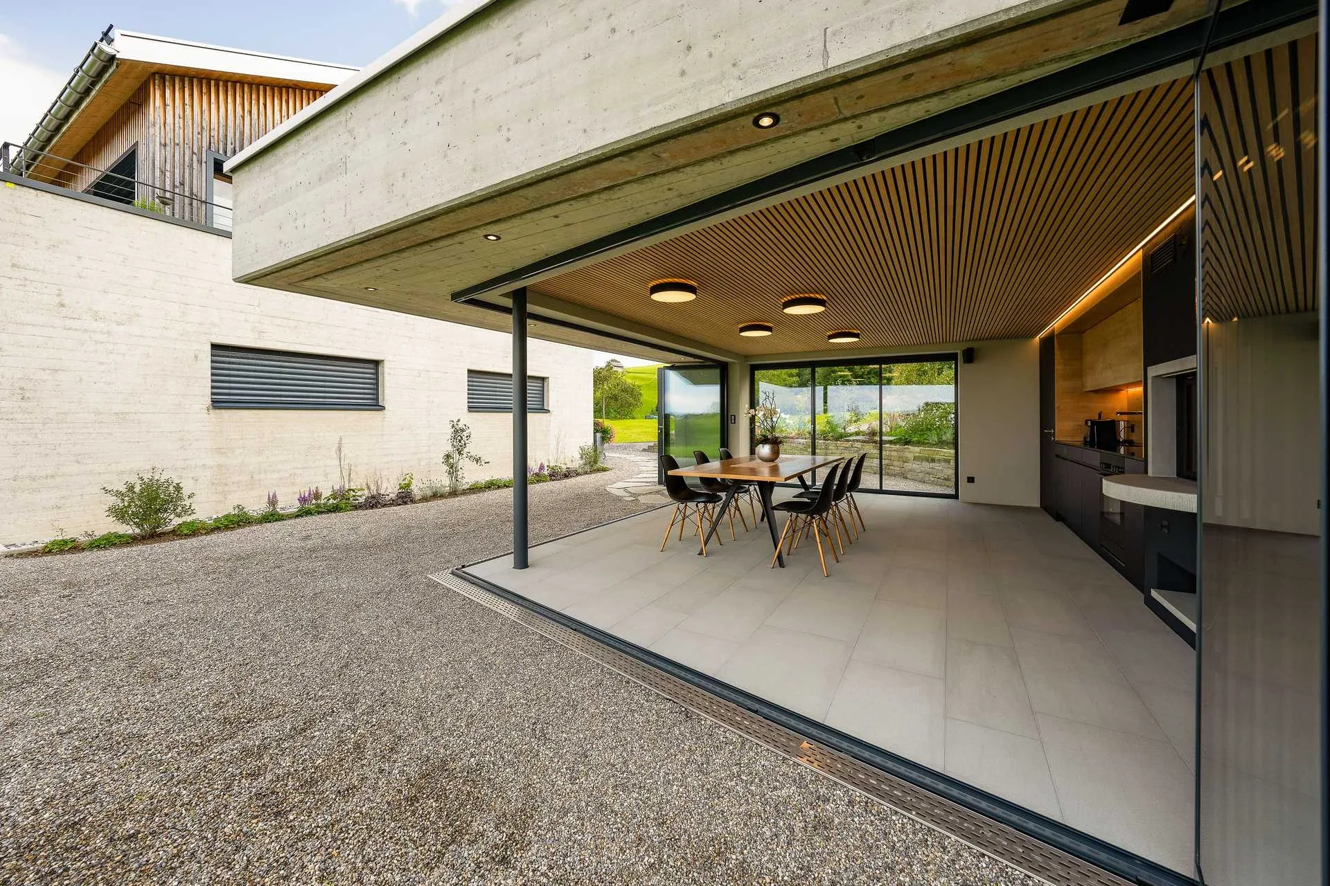 Pavillon Eckansicht mit Sichtbeton-Decke und Holzlamellen-Untersicht, Haupthaus im Hintergrund