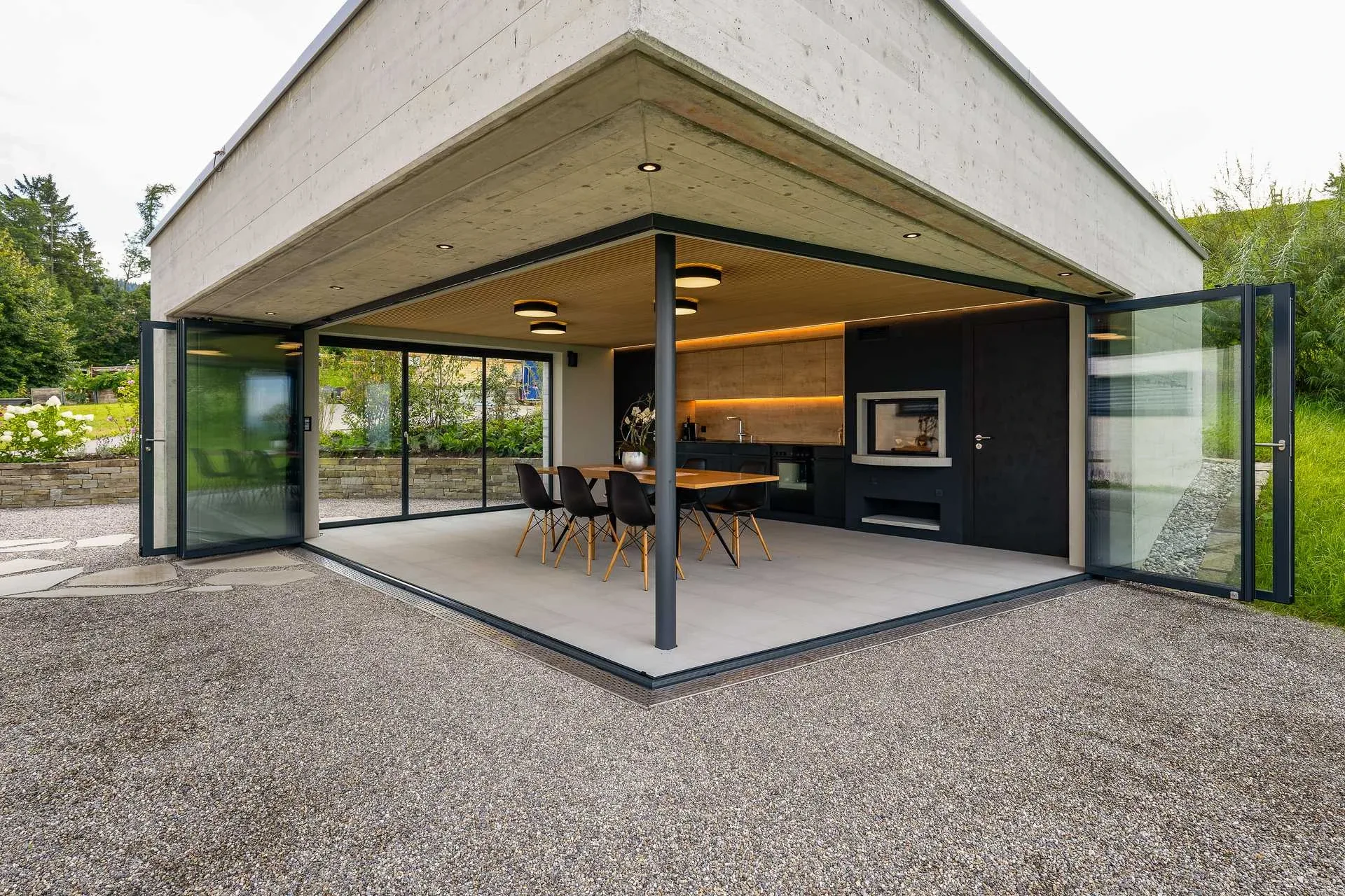 Pavillon Eckansicht mit weit geoeffneter Schiebe-Dreh-Verglasung, Esstisch und Kueche sichtbar