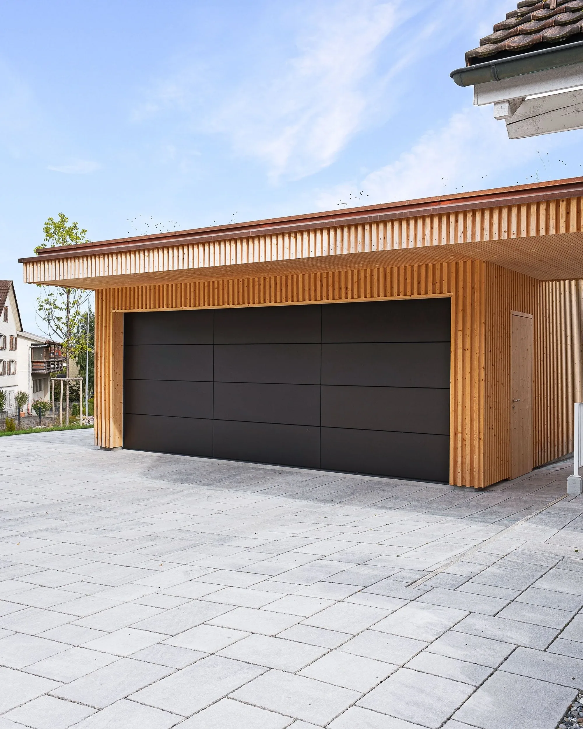 Seitlichen Bllick auf einen angebauten, geschlossenen Carport aus Holz und einem anthrazitfabenes Sektionaltor von Hörmann