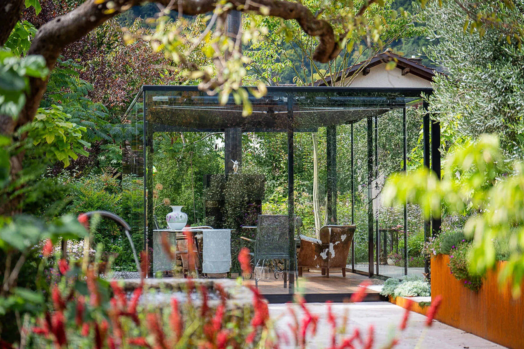 Glaslounge im Garten mit bluehenden Blumen im Vordergrund